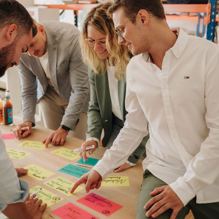 Fünf Personen diskutieren und arbeiten an einem Tisch mit bunten Notizen.