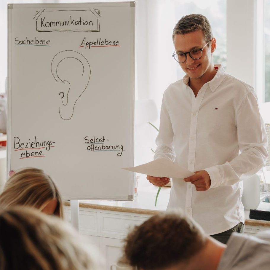 Mann mit Brille präsentiert ein Konzept zur Kommunikation vor einer Gruppe.