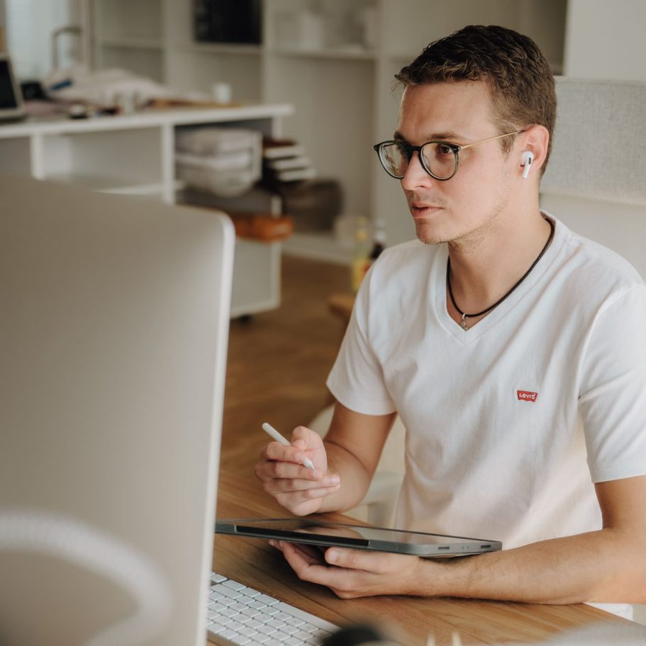 Junger Mann mit Brille sitzt am Schreibtisch und arbeitet am Laptop.