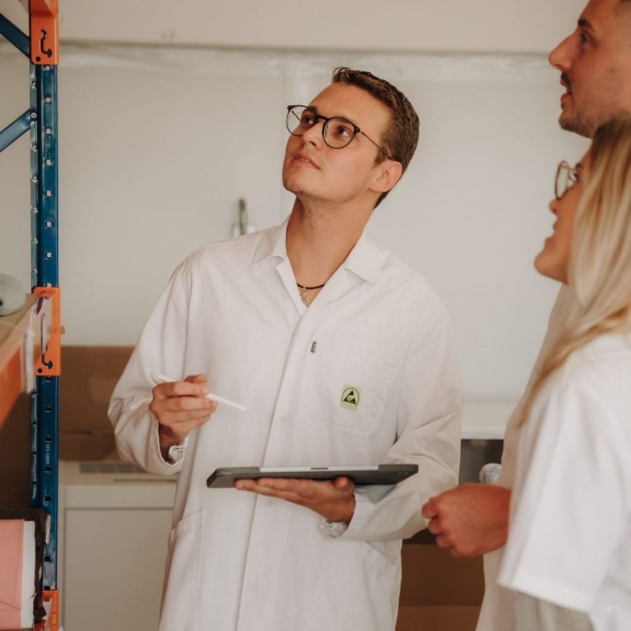 Besprechung in einem Labor, drei Personen in weißen Kitteln, einer mit Tablet.